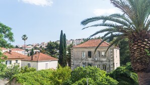 A building with a red-tiled roof, surrounded by lush greenery and palm trees. - Katarina rooms - twin room (Dubrovnik)