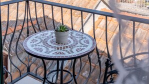 Ein Balkon mit Tisch und Blumentopf, mit Blick auf ein Gewässer und eine hügelige Landschaft.