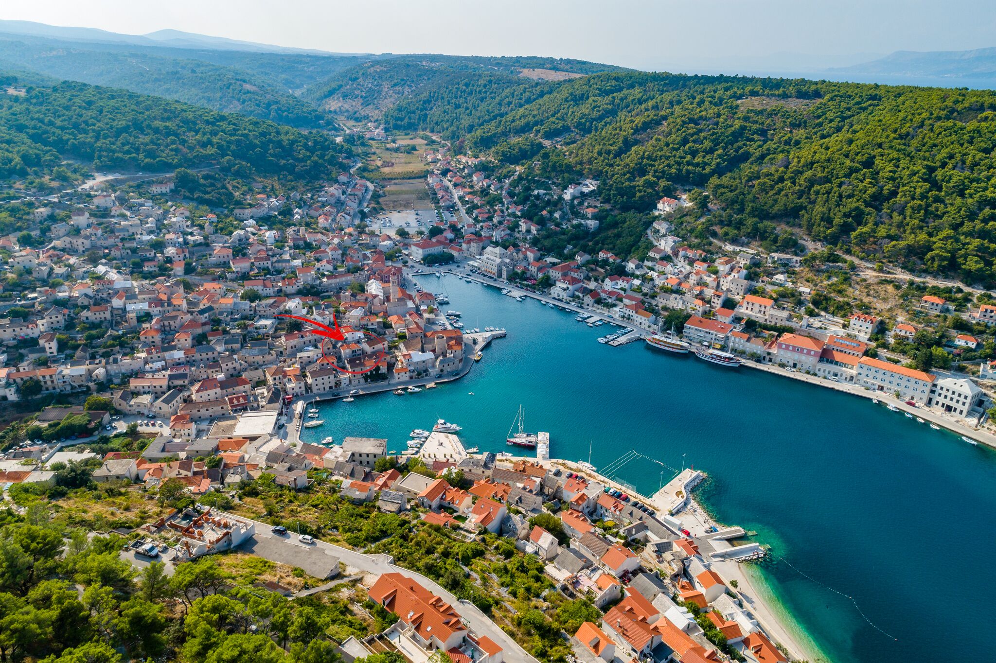 An aerial view of a coastal town with a marina, dense housing, and surrounding hills.