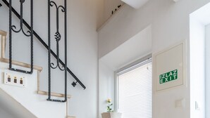Eine Treppe mit beigen Stufen und schwarzen Metallgeländern, ein Fenster mit Rollläden und ein Ausgangsschild an der Wand.