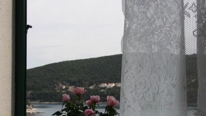 Ein Blumentopf mit rosa Blüten auf einem Fensterbrett, mit Blick auf die Küste, Häuser und Hügel.