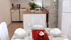 Comedor con una mesa dispuesta para cuatro, incluyendo platos, cubiertos y copas de vino. Un camino de mesa rojo divide la mesa, y un pequeño objeto decorativo se encuentra en el centro.