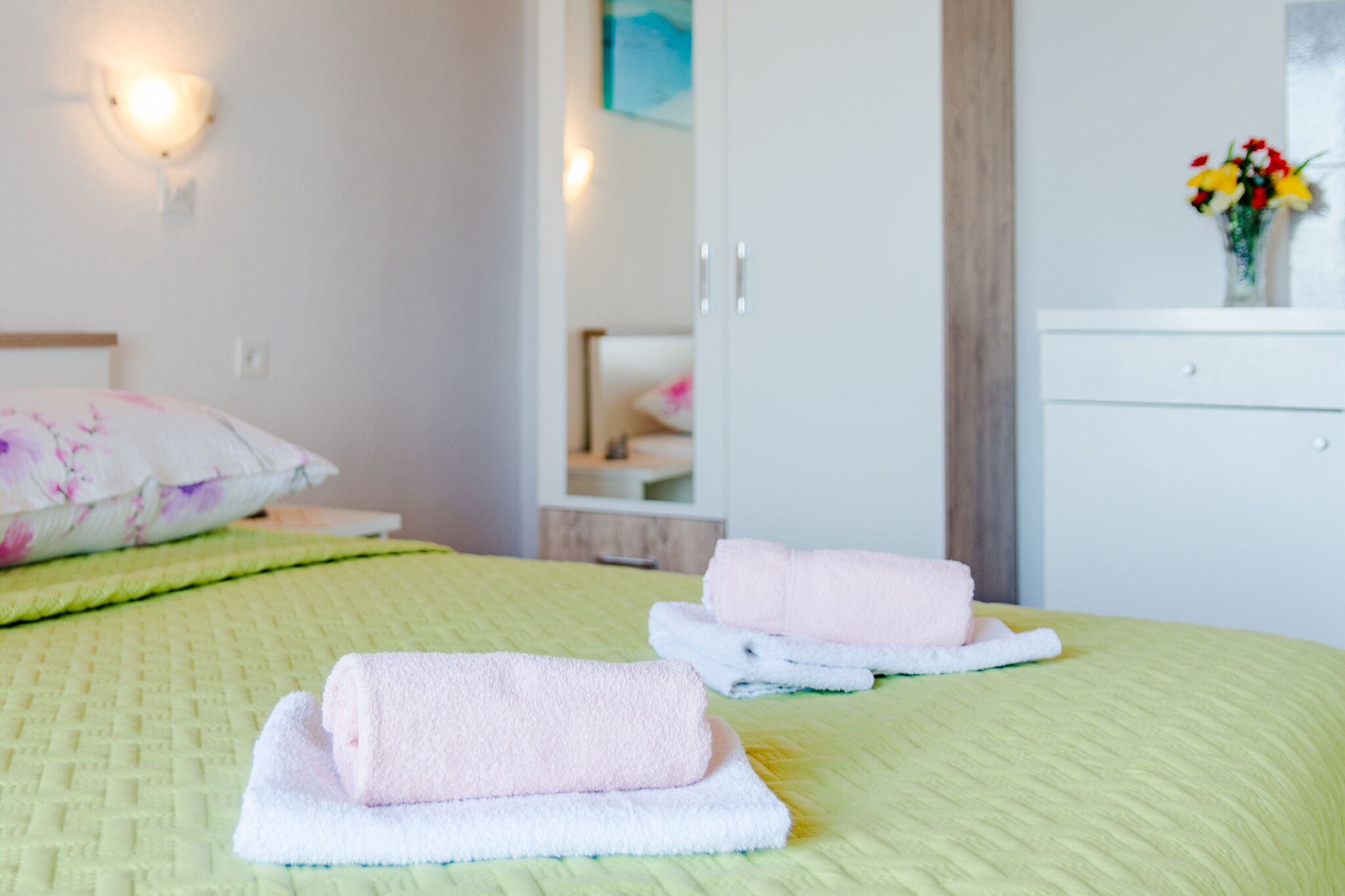 A neatly made bed with green bedding and two folded towels.