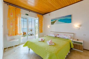 Un dormitorio con cubrecama verde, dos almohadas, una mesita de noche y un cuadro con una escena de playa.
