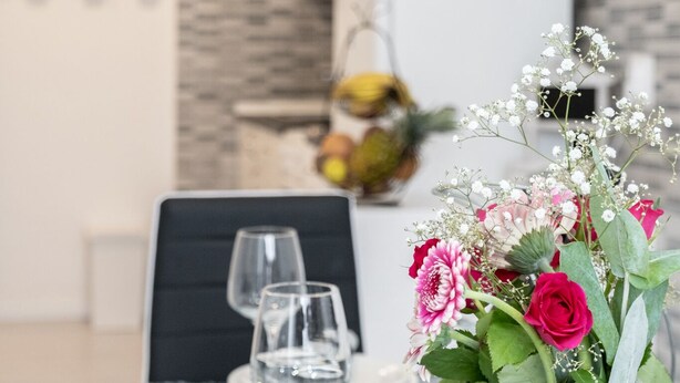 Een eettafel gedekt met witte borden, servetten en een vaas met bloemen.