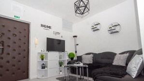 Een moderne woonkamer met een bank, een televisie, een witte boekenkast met planten en een geometrische lamp.