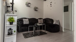 Een moderne woonkamer met een zwarte leren bank, een metalen salontafel en decoratieve muurkunst.