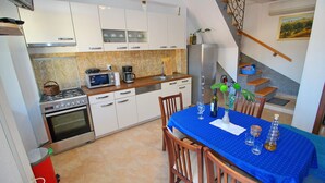 A modern kitchen with white cabinets, a dining table with a blue tablecloth, and a staircase leading to a loft area. - Apartment Mambo , Mljet - Duplex Apartment with Terrace and Sea View (Sobra)
