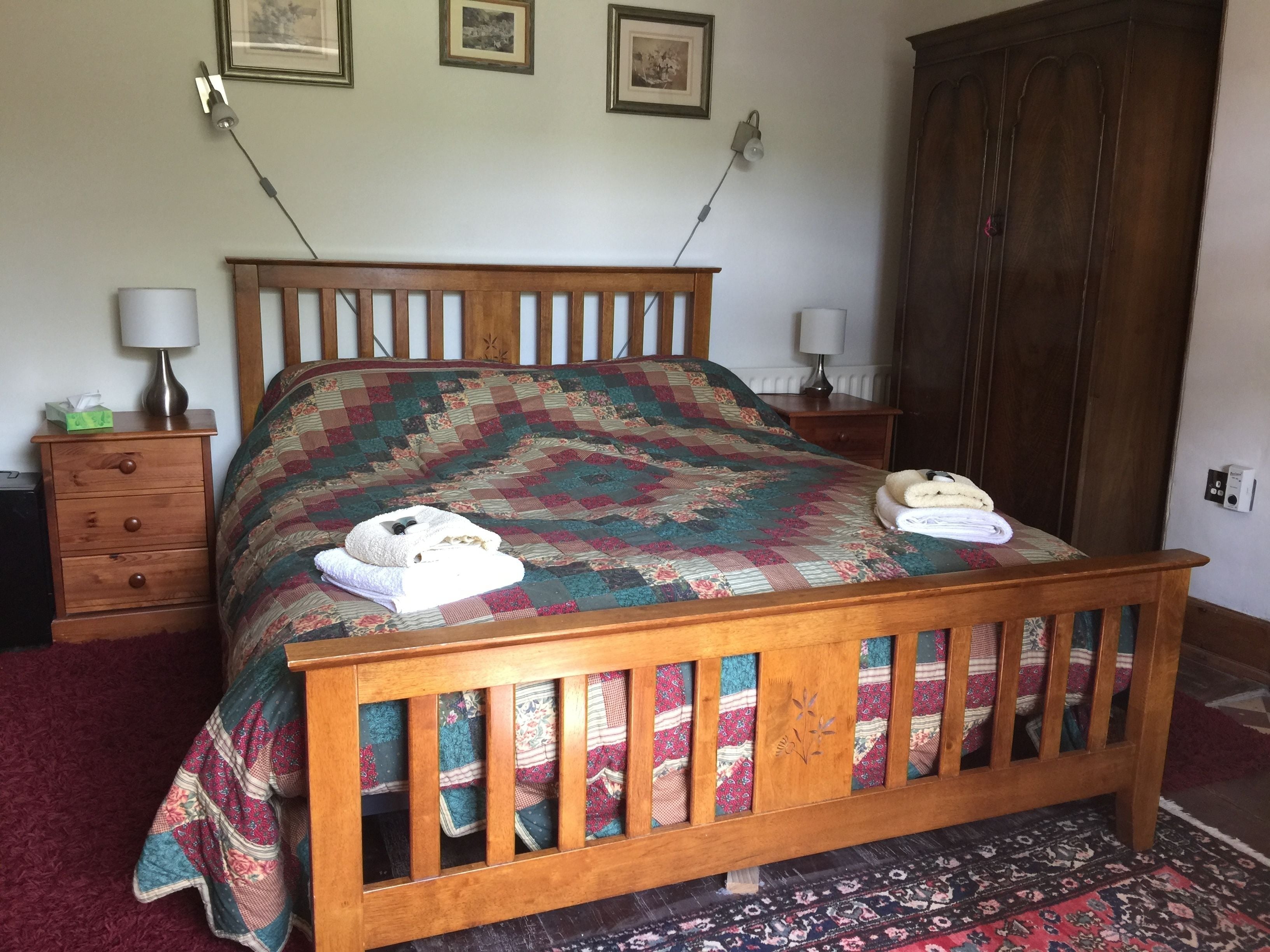 Una cama de madera con colcha colorida, una mesita de noche con lámpara y un armario.