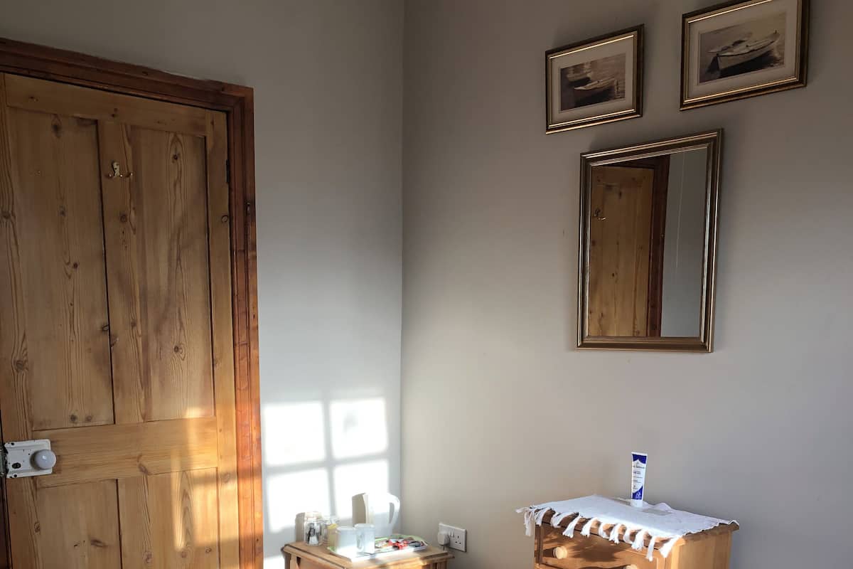 Un dormitorio con un armario de madera, una mesita de noche con lámpara, un tocador y una cama con colcha estampada.