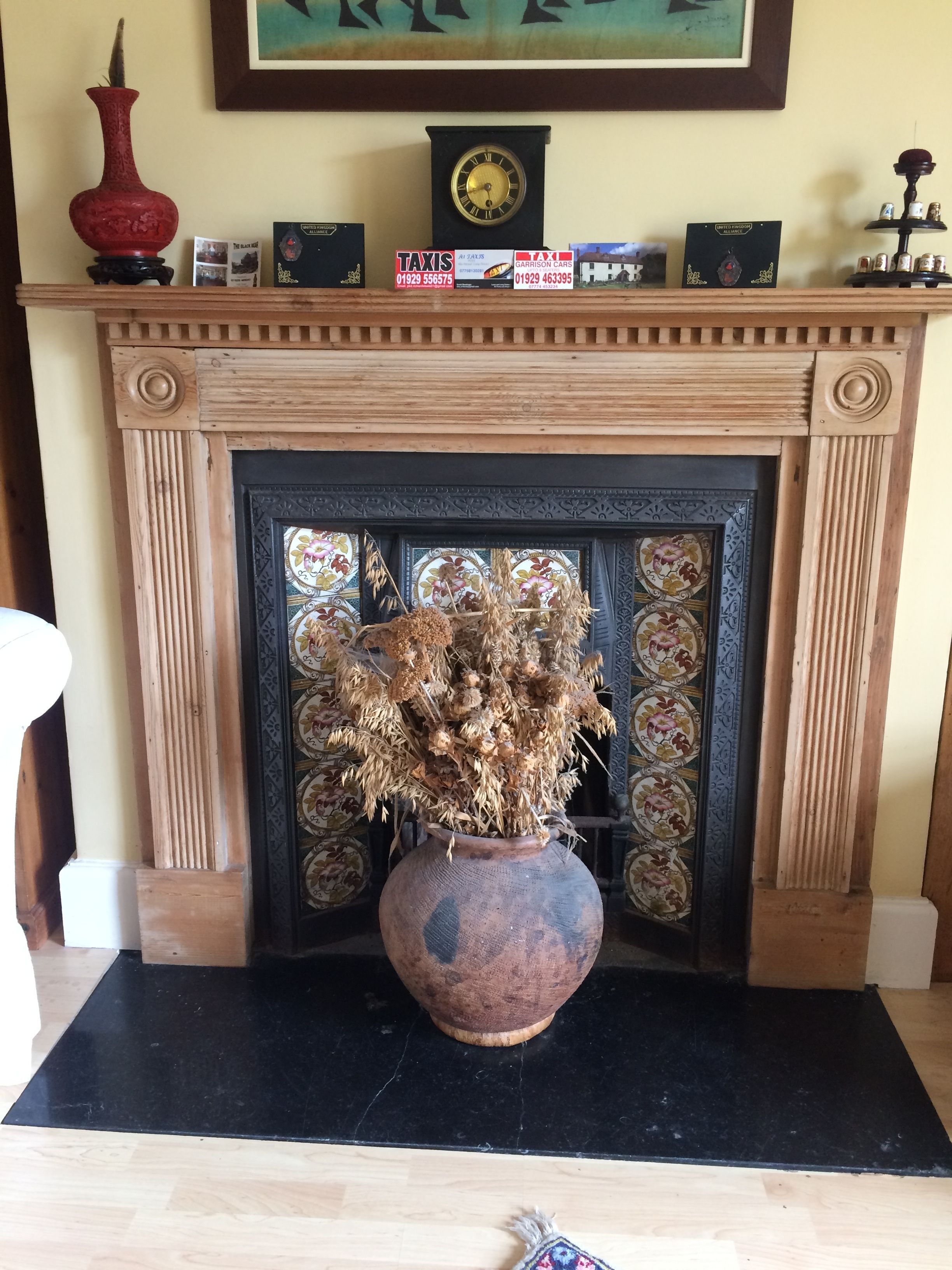 A fireplace with a vase of dried flowers, a clock, and several signs on the mantel.