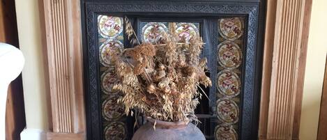 A fireplace with a vase of dried flowers, a clock, and several signs on the mantel.