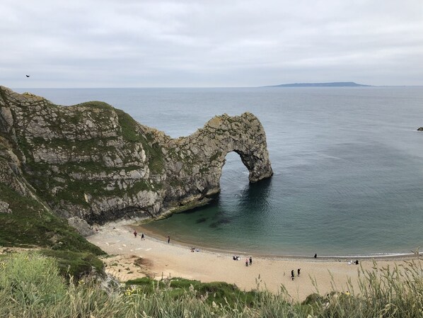 Eine Küstenlandschaft mit einer natürlichen Felsformation, einem Sandstrand und freiem Blick auf das Meer.