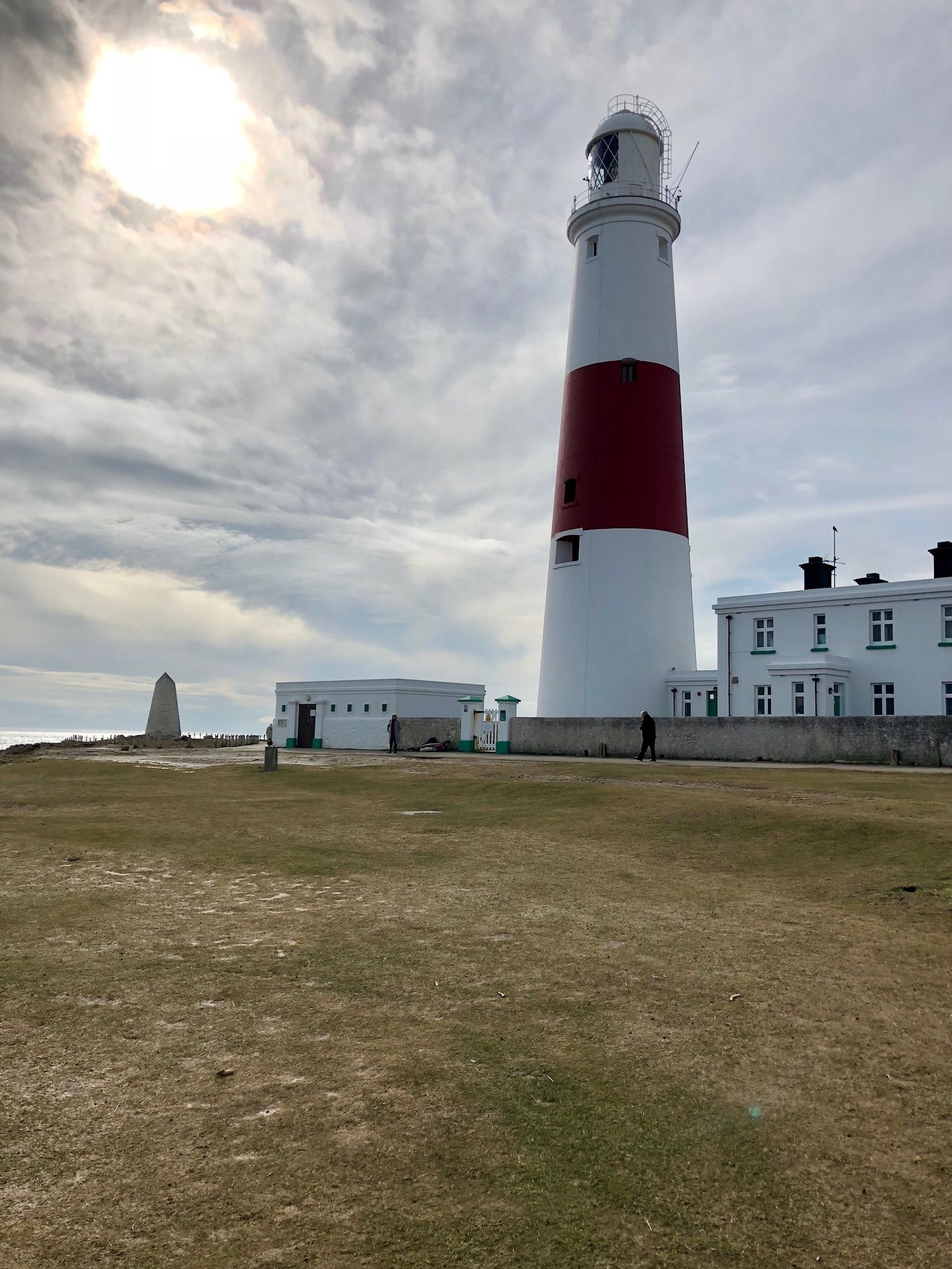 A lighthouse with a red and white structure, a small building with a green roof, and a grassy area in front.