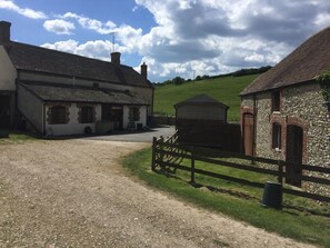 A rural setting with a gravel driveway leading to a white building with a black roof, a stone building with a red roof, and a wooden shed. - Belhuish Farmhouse (Wareham)