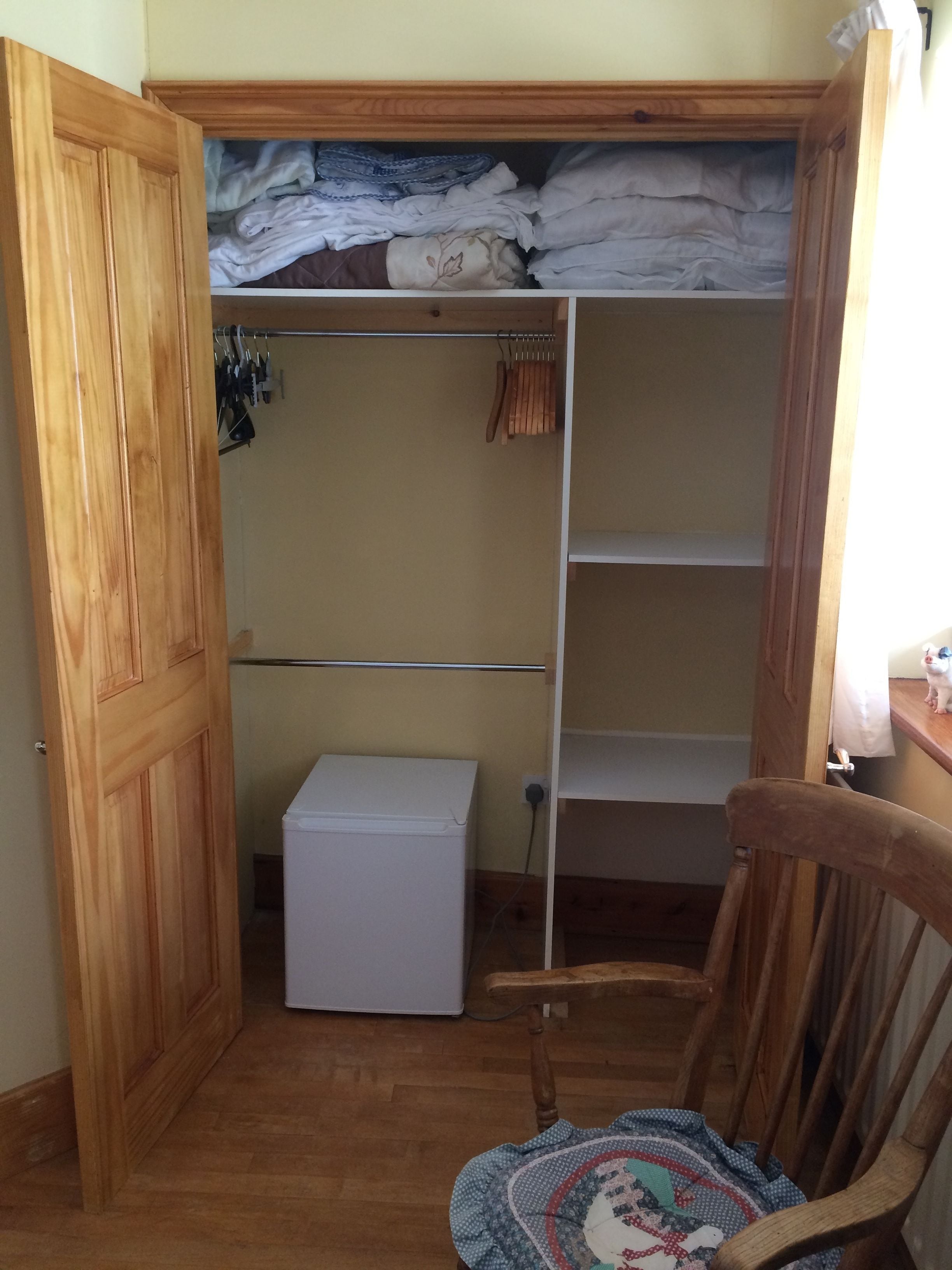 A compact room with a wooden wardrobe, a small white appliance, and a wooden chair.