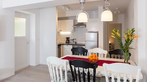A modern kitchen with white cabinets, a stainless steel range hood, and a dining area with a red table runner and a bowl of fruit. - Apartment Rea Zaton - Two-Bedroom Apartment (Zaton)