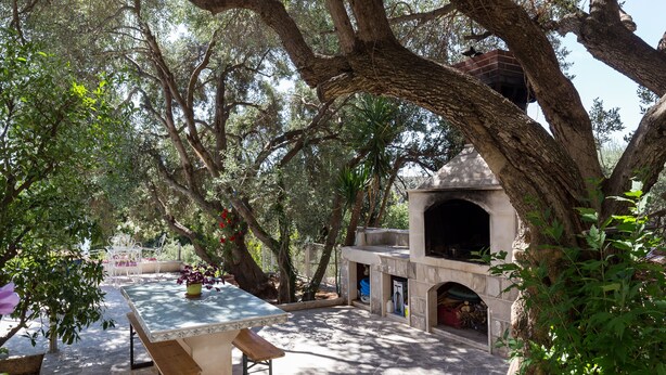 An outdoor patio area with stone flooring, a table with chairs, and a stone oven structure. - Apartment Rea Zaton - Two-Bedroom Apartment (Zaton)