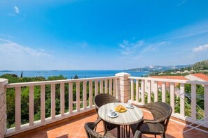 Ein Balkon mit Korbmöbeln, einem Tisch mit Speisen und einem weiten Blick auf Meer und Hügel.