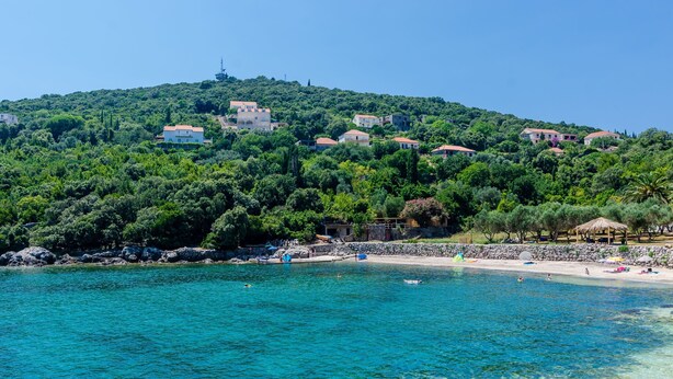 Una zona costiera con acque turchesi cristalline, una spiaggia sabbiosa e edifici su una collina.