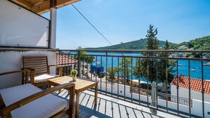 Un balcone con mobili in legno, vista sul mare e paesaggio montuoso.