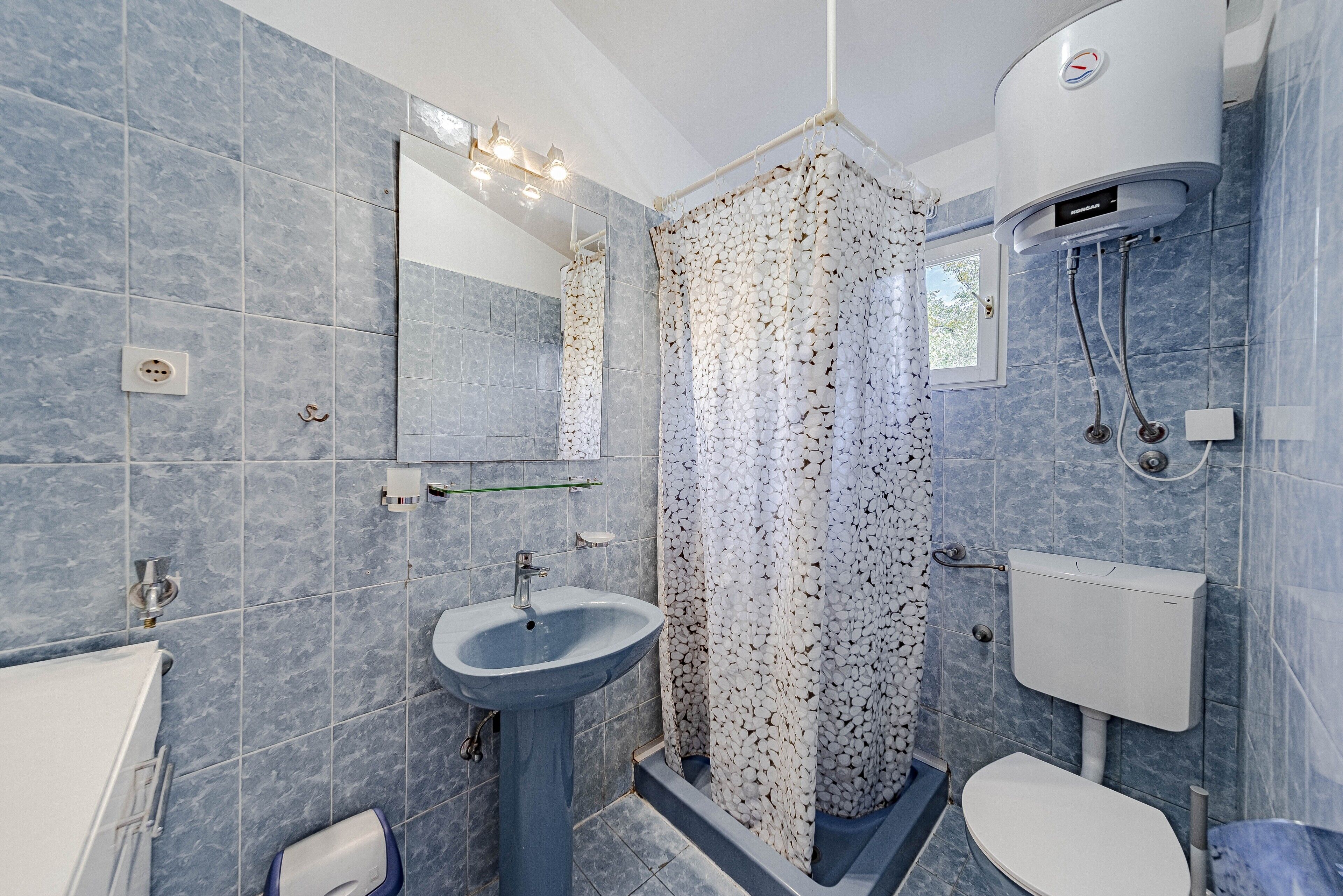 A bathroom with a pedestal sink, a toilet, a shower with a white and black patterned curtain, and a wall-mounted water heater.