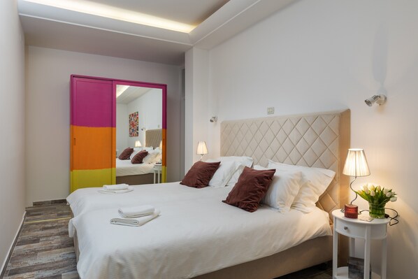 Una cama bien tendida con sábanas blancas y almohadas marrones, una lámpara de noche y una mesita con un florero.