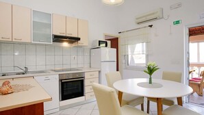 A modern kitchen with white cabinets, a built-in oven, and a dining area with a round table and chairs.