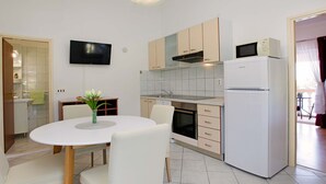 A modern kitchen with white cabinets, a built-in oven, a microwave, and a refrigerator. There is a dining table with chairs and a vase of flowers.
