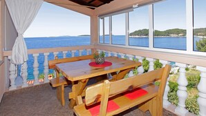 A wooden table and bench set on a balcony with a view of the sea.