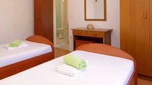 A hotel room with two beds, a wooden wardrobe, a wooden desk with a mirror, and a bathroom visible through an open door.