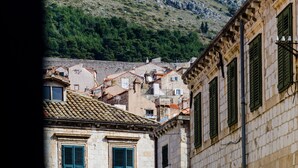 A stone building with green shutters and a tiled roof, part of a hillside village.