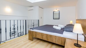 A bedroom with a skylight, a bed with pillows, a bedside table with a lamp, and a wooden floor.