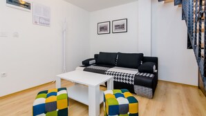 A modern living room with a black and white patterned sofa, a white coffee table, and colorful ottomans. There is a staircase with a metal railing to the right.