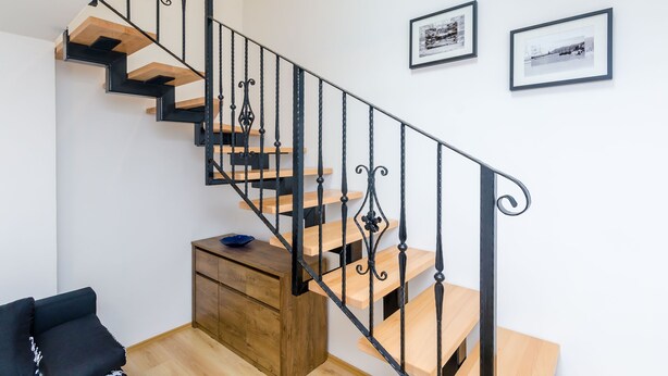 A modern staircase with black railings and wooden steps, leading to a landing with a small wooden cabinet and a blue bowl.