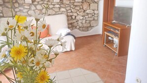 Una sala de estar con pared de piedra, un sofá blanco, un mueble para televisión y un jarrón con flores.