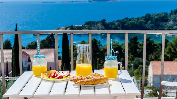 Une table dressée avec des aliments et des boissons pour le petit-déjeuner, placée sur un balcon offrant une vue panoramique sur la côte.