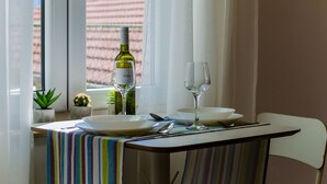 Une table à manger avec une bouteille de vin blanc, deux verres et des assiettes, le tout placé devant une fenêtre ornée de rideaux.