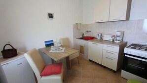 Een praktische keuken met een koelkast, koffiezetapparaat, fornuis en een eettafel met stoelen.