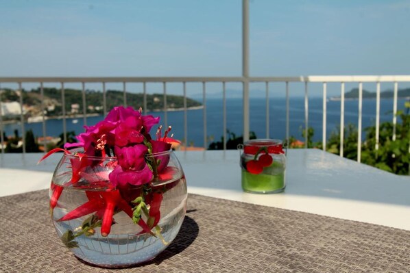 Un cuenco de vidrio con flores rosadas en un balcón con vistas al mar.