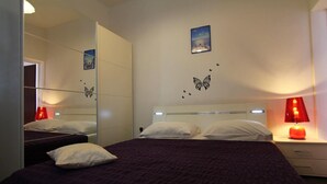 Een slaapkamer met een grote spiegel, twee bedden, een nachtkastje met een lamp en vlinderstickers op de muur.