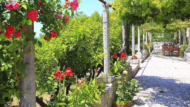 A garden with a pergola, stone pathway, and a table with chairs. - Superior Double Room with Balcony and Sea View (Soba 3) (Orasac)