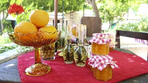 A table with a glass bowl of oranges, small bottles, and jars of honey on a red cloth. - Superior Double Room with Balcony and Sea View (Soba 3) (Orasac)