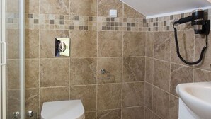 Een badkamer met beige tegels, een douche en een haardroger bevestigd aan de muur.