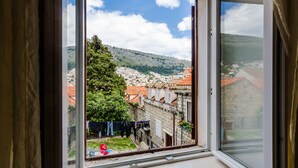 Vista pela janela de uma cidade com edifícios, uma árvore e uma bandeira vermelha no chão.