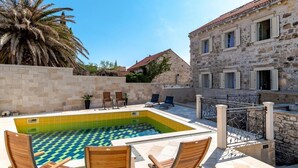 A pool area with a tiled floor, lounge chairs, and a stone building with windows. - Rooms Miron - Deluxe Double Room with Balcony and Sea View (Sumartin)