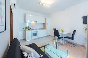 A modern living room with a glass coffee table, black sofa, and a dining area with a white table and black chairs.