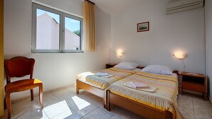 Un dormitorio con dos camas, una silla, un ventanal y aire acondicionado.