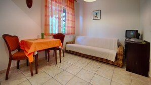 Un comedor con mesa y sillas, un sofá, un televisor y una ventana con cortinas.