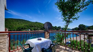 Un balcón con mesa y sillas, con vista a un cuerpo de agua y vegetación.